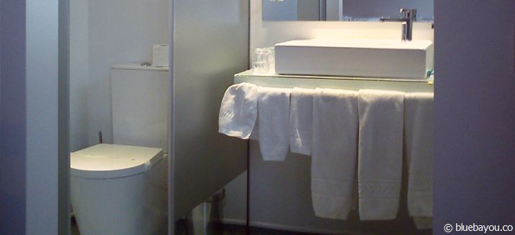 An open bathroom at a hotel in Portugal: View from the bed towards the toilet which hides behind glass.